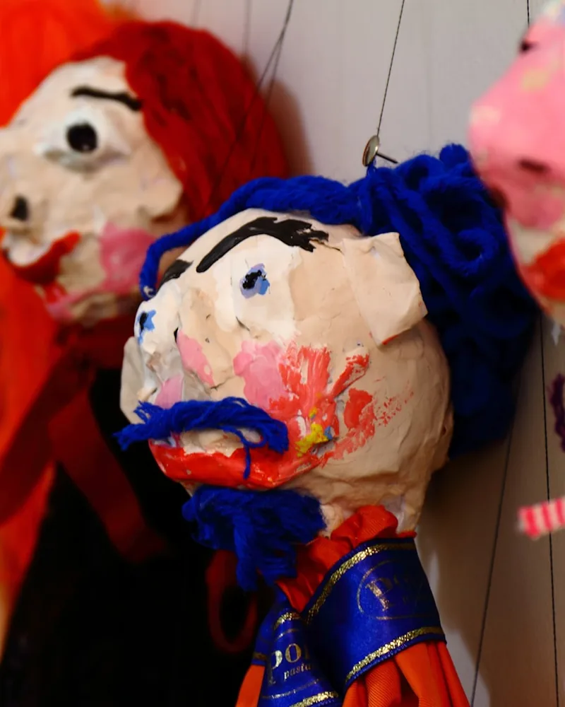 Cabezas de títere de cartón piedra pintadas a mano, con cabello de lana, colgadas en el taller