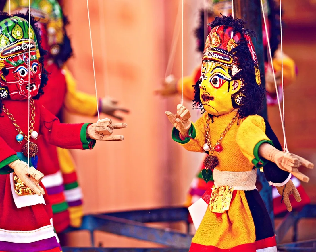 Dos marionetas de hilos con cabezas talladas y trajes de tela colgadas de sus crucetas